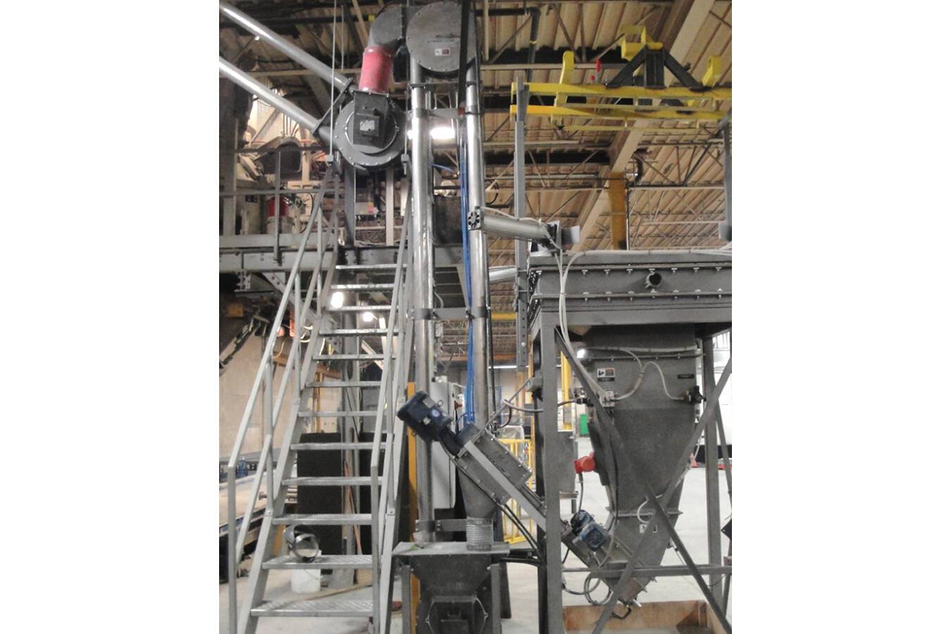 A vertical Aero Mechanical Conveyor moves cement powder from dual Flexible Screw Conveyors to a second Aero Mechanical Conveyor that extends through the building roof to an outdoor storage silo.